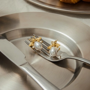Macro detail of gold bee earrings with teardrop pearls displayed on a metal fork