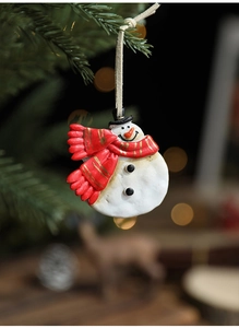 Macro detail of hand-painted resin snowman ornament hanging on green pine branches
