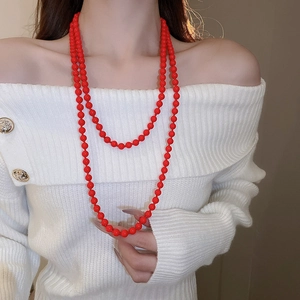 Detail of elegant double-layered long red faux pearl necklace worn with a white sweater