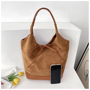 Brown suede tote bag detail with leather handle and decorative knot on a white platform