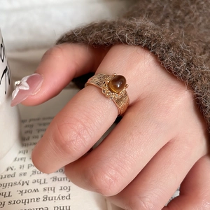 Close-up of gold-plated tiger eye ring with ribbed band and small crystals on a hand