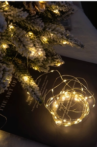 Detail of warm white LED copper wire fairy lights wrapped on snowy Christmas tree branches