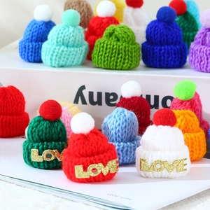 Close-up of mini knitted Christmas hats with colorful yarn and LOVE patches for DIY crafts