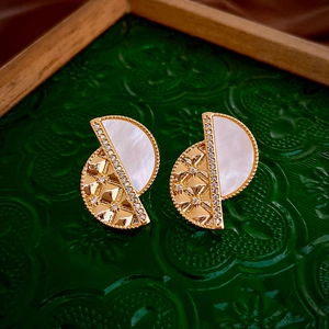 Detail of semi-circular gold earrings with mother of pearl and zircon on glass tray