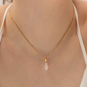 Golden beaded chain necklace with geometric pink crystal pendant worn by a model