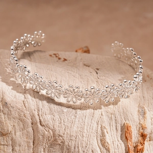 Close-up of polished silver hollow flower cuff bracelet on a natural stone base