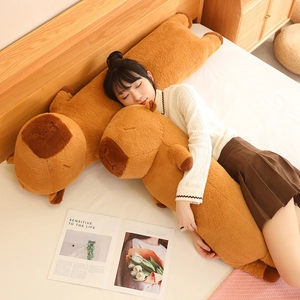 Close-up of a long, soft plush capybara body pillow held in a cozy bedroom setting