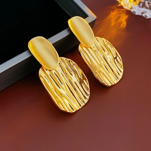 Gros plan de boucles d'oreilles géométriques dorées avec texture ondulée et brossée