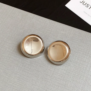 Macro shot of polished silver button earrings on textured surface with a card