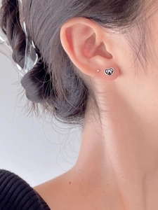 Close-up of black heart earrings with silver bow detail worn on model's ear