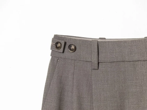 Detail of tailored taupe suit trousers featuring side adjustment buckles and dual button waist
