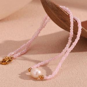 Pink beaded necklace with large freshwater pearl and golden accents on a wooden spoon