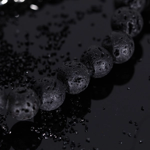 Macro shot of natural porous black lava stone beads on a sleek mirror surface