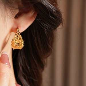 Detailed close-up of golden geometric hollow cage earrings on a model’s ear