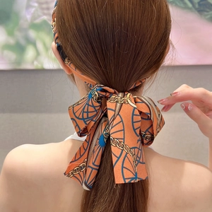 Close-up of silk bow hair ribbon with orange chain pattern tied on a ponytail