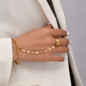 Detail of gold star sequin hand chain bracelet connected to a wide band ring for women