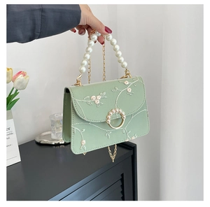 Detailed view of light green crossbody bag with floral embroidery and large pearl handle