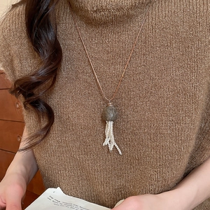 Long tassel necklace with dark gemstone and pearls on a brown sweater background