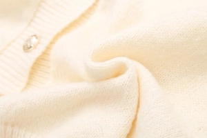 Makroansicht des weichen cremefarbenen Strickstoffs und des silbernen Knopfs der Strickjacke