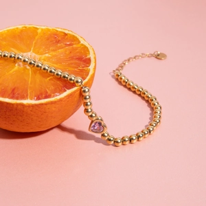 Detail of 18K gold beaded bracelet with pink heart zircon on a fresh orange background