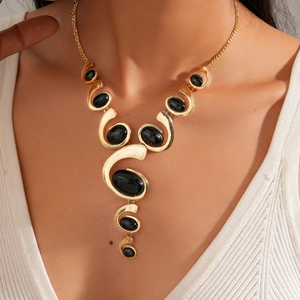 Detail shot of the gold spiral necklace with black oval resin stones worn by a model