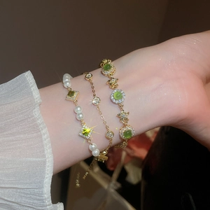 Macro detail of layered gold bracelets with green zircons, cat eye stones and pearls