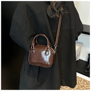 Rear view of dark brown glossy crossbody bag with adjustable strap and embossed detail