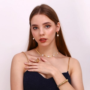 Macro detail of gold-plated butterfly necklace and pearl earrings on model