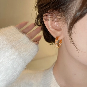 Close-up of woman wearing gold hoop earrings set with orange and white zircons