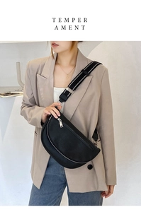 Close-up of black crescent crossbody bag with white striped strap on beige blazer