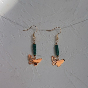 Detail of 18K gold butterfly earrings with green natural stone beads on a textured surface
