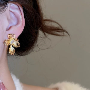 Detailed view of a gold flower earring with cubic zirconia on a model's ear