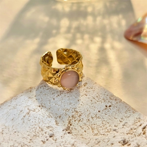 Detail of gold geometric ring featuring a pink opal stone and quilted metal texture