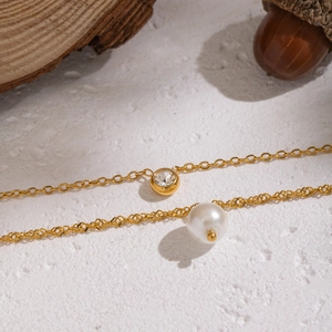 Macro detail of a double-layered gold necklace with a pearl and zircon stone