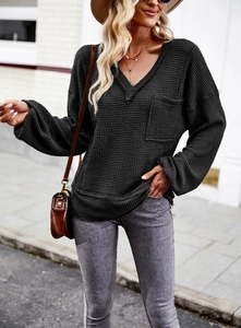 Detail view of the black V-neck waffle knit sweater featuring a functional chest pocket