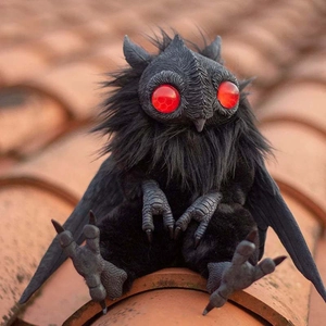Κοντινό πλάνο μαύρου βρεφικού λούτρινου Mothman με μεγάλα κόκκινα μάτια στη στέγη