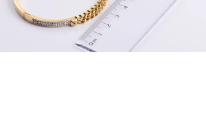 Detail view of a gold bangle width measurement showing paved crystals and chain link