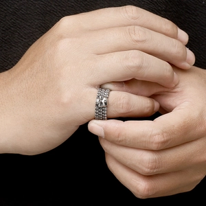 Detail of vintage silver skull ring with chain texture worn on hand on dark fabric