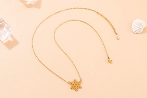 Flat lay of a gold snowflake pendant necklace on a warm peach background with ice props