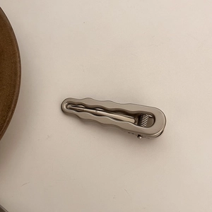 Minimalist silver wavy metal hair clip with spring mechanism on cream background