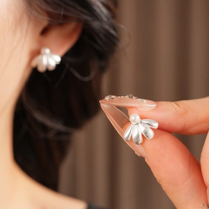 Macro shot of silver shell earrings with pearls held by model for detail display