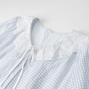 Detail of blue gingham shirt featuring white lace collar and delicate neckline tie