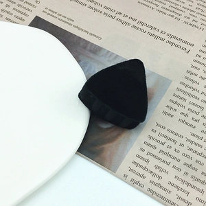 Detail of a small black flocked triangular hair clip on a white plate with newspaper