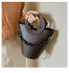 Detail of a dark brown bucket bag featuring a round handle and resin chain decoration