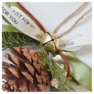 Detail of Christmas ornament with pine cone, gold bells, and green ribbon on white background