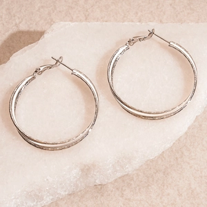 Detailed macro view of silver textured double layer hoop earrings on white stone background