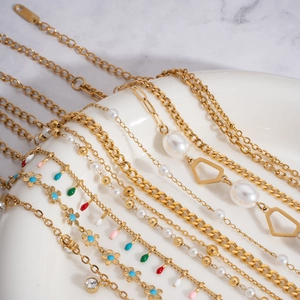 Flat lay of gold layered pearl anklets with floral charms on white ceramic plate