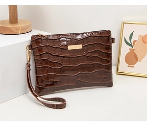 Detail of dark brown faux crocodile leather clutch with gold metal plaque and wristlet strap