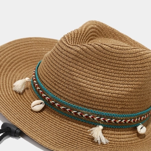 Close-up of bohemian straw sun hat with woven ribbon, sea shells and tassel detail