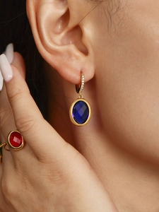 Close-up of elegant blue oval gemstone earrings and matching red crystal ring on model
